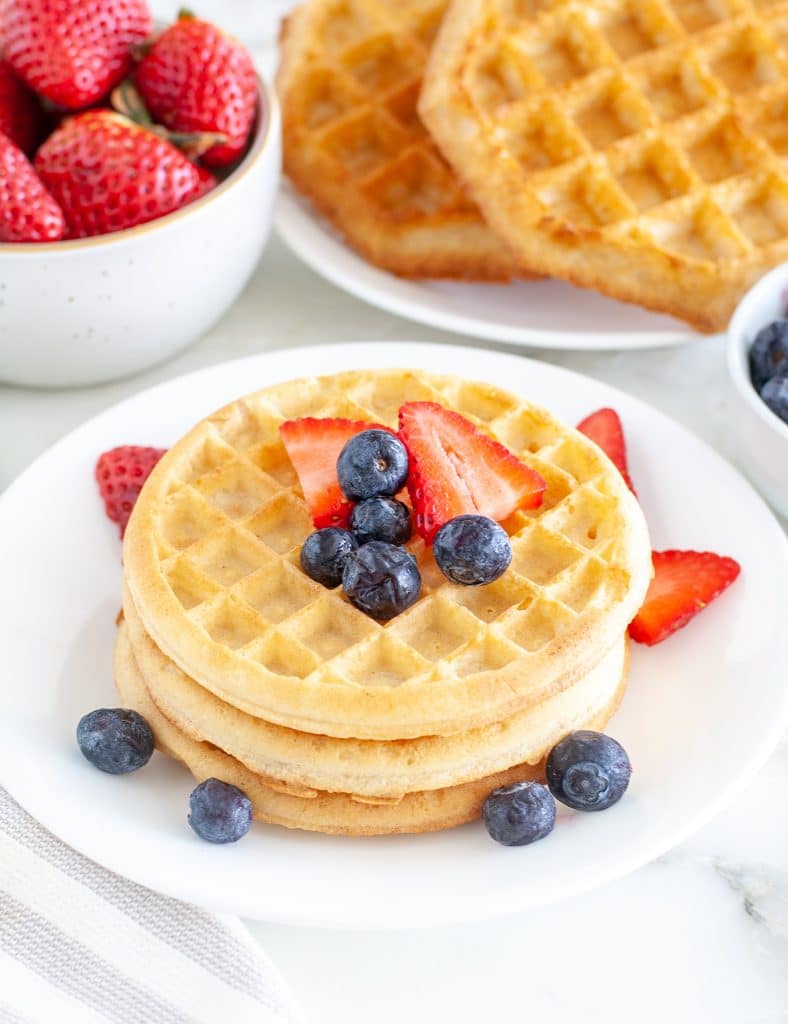 Waffles stacked on plate with berries.