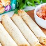Cooked taquitos on a board with bowl of salsa.