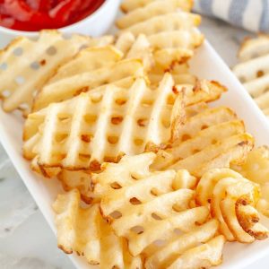 Waffle fries on a plate with bowl of ketchup.