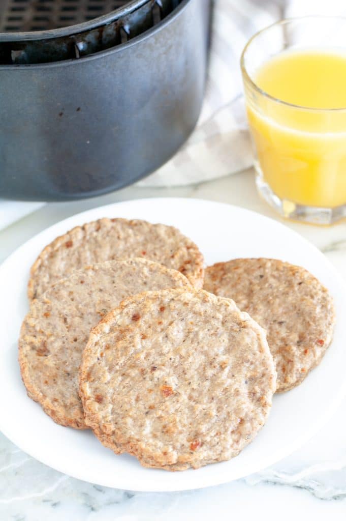 Plate with cooked breakfast sausage patties and glass of orange juice. 