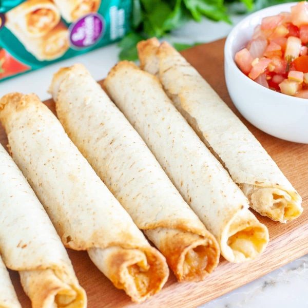 Cooked taquitos on a board with bowl of salsa.