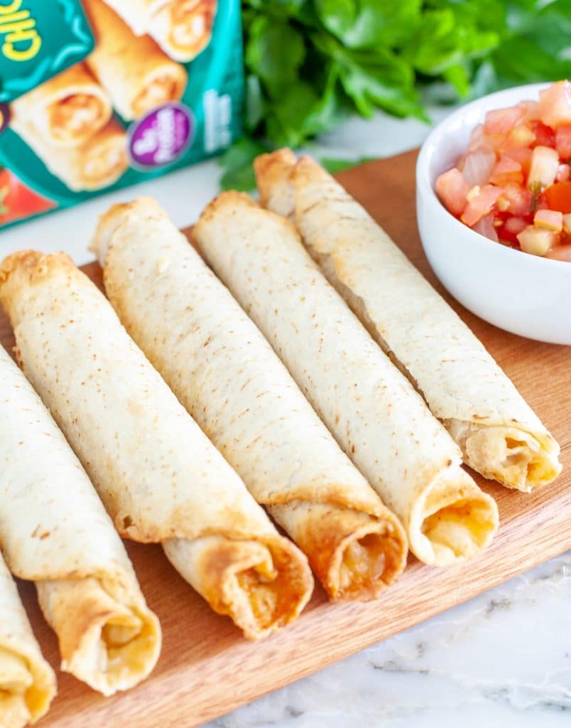 Taquitos on cutting board with bowl of salsa. 