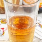 Glass with drink beside playing cards.