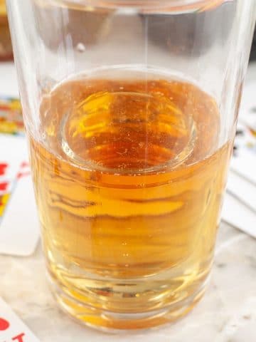 Glass filled with energy drink and playing cards beside the glass.
