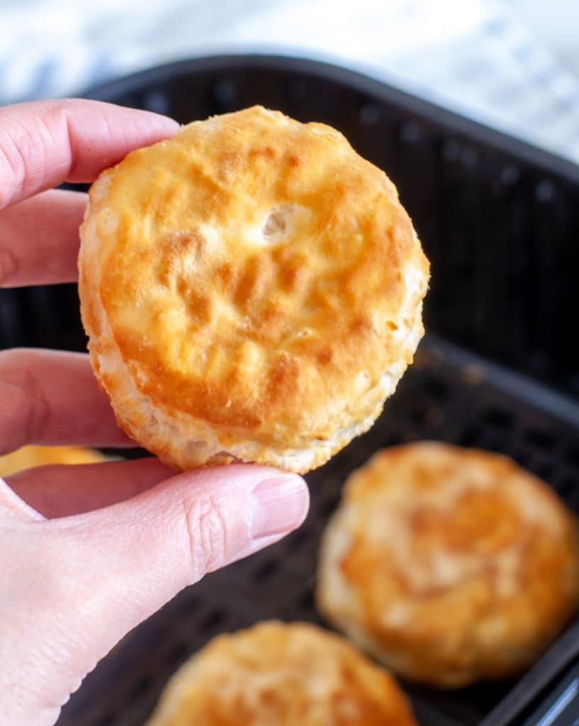 Hand holding biscuit over air fryer basket. 