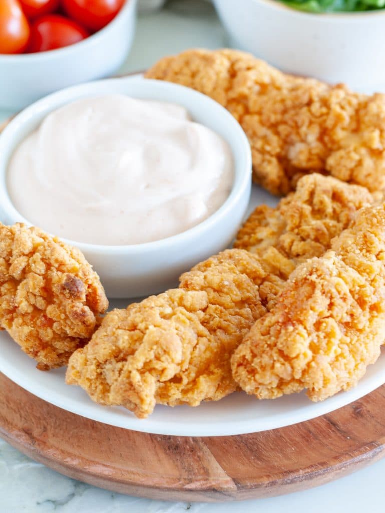 Chicken tenders on a plate with bowl of white sauce.