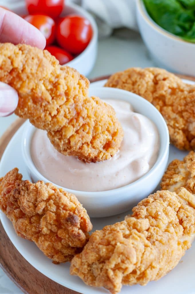 Hand holding chicken tender dipping it into sauce. 
