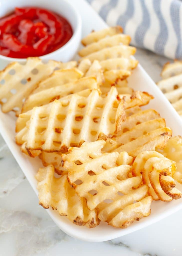 Waffle fries on a plate with bowl of ketchup. 