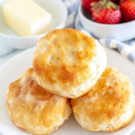 Three biscuits on a plate with bowl of butter and strawberries.