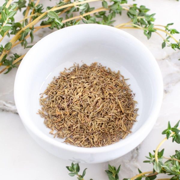 Dried thyme in a bowl with fresh thyme on a table.