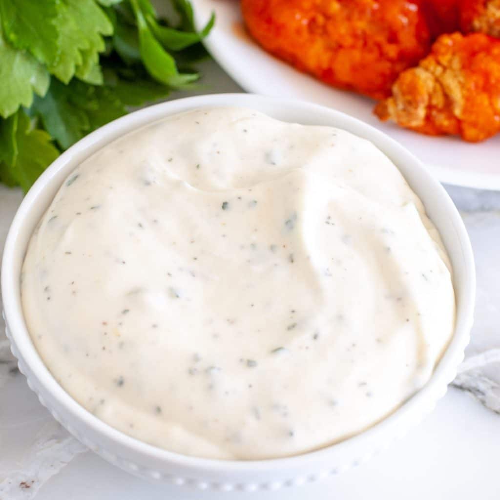 Bowl of ranch dressing with wings in background. 