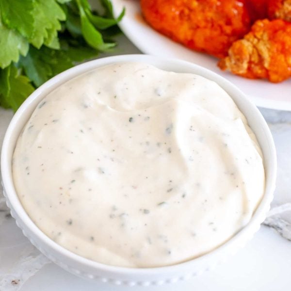 Bowl of ranch dressing with wings in background.