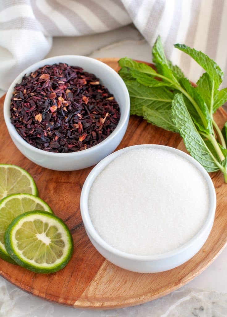 Bowl of hibiscus flowers, sugar, mint leaves and lime.