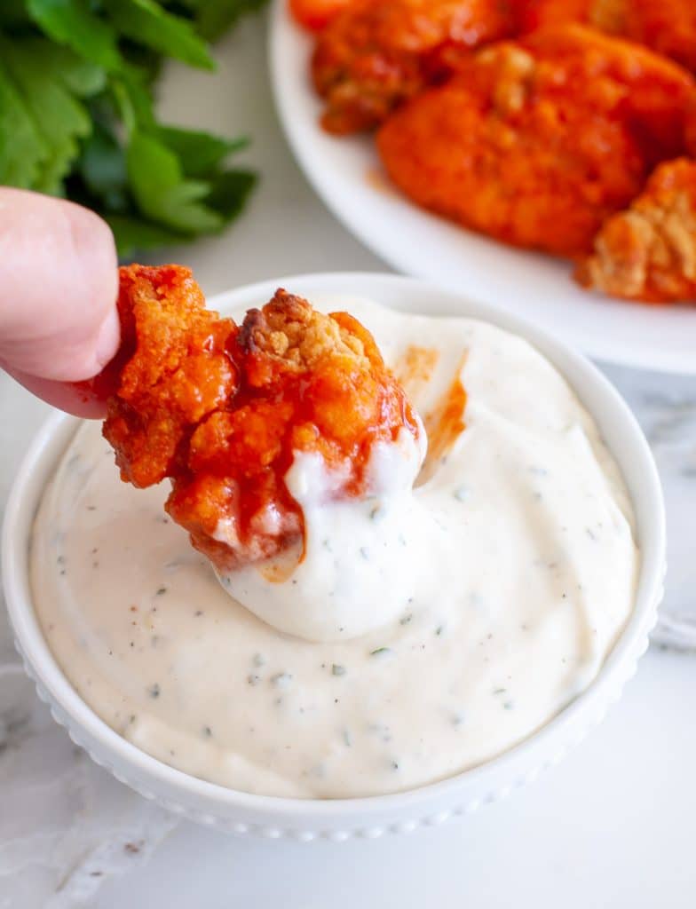 Hand dipping chicken in ranch. 