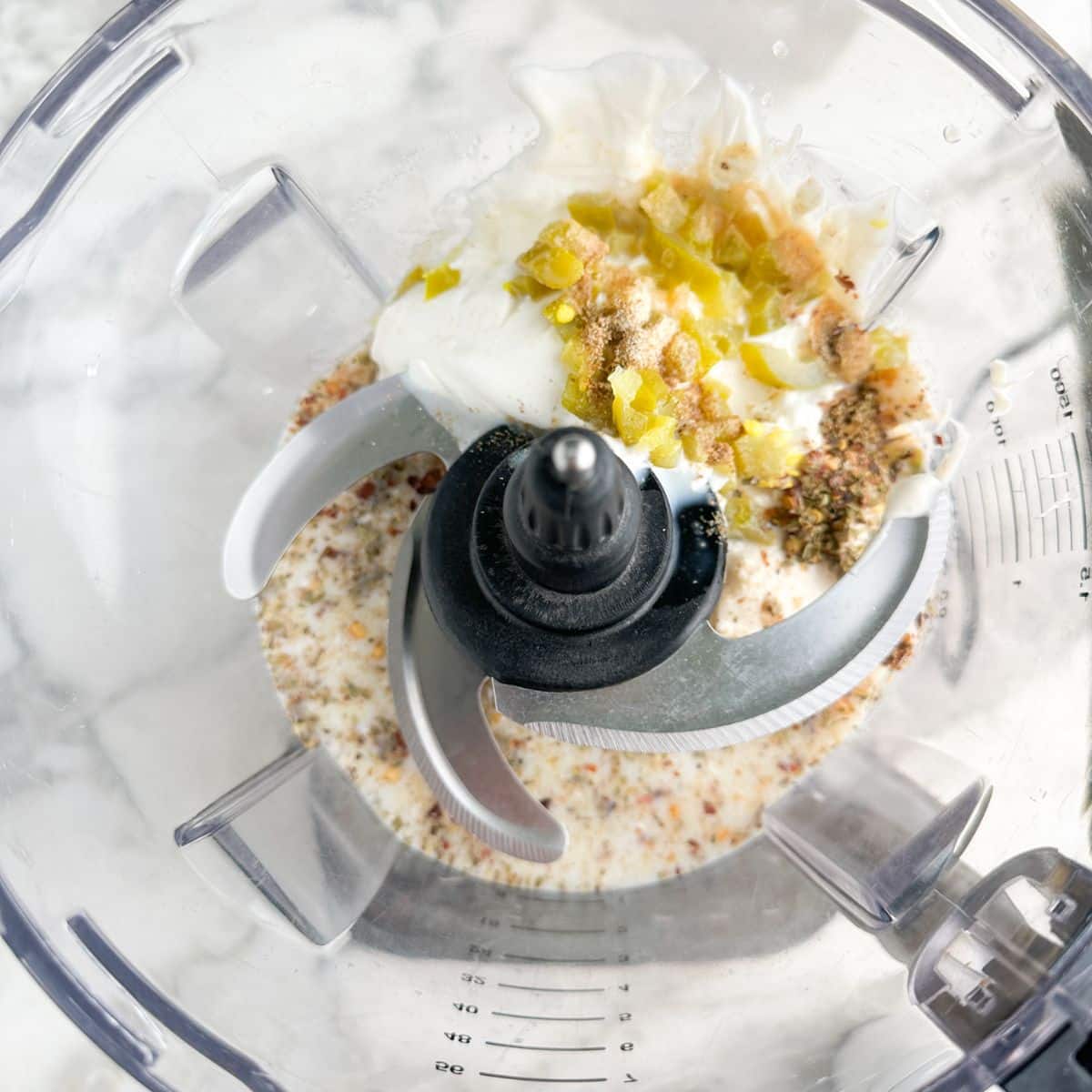 Food processor with mayonnaise, seasonings, milk, and jalapenos. 