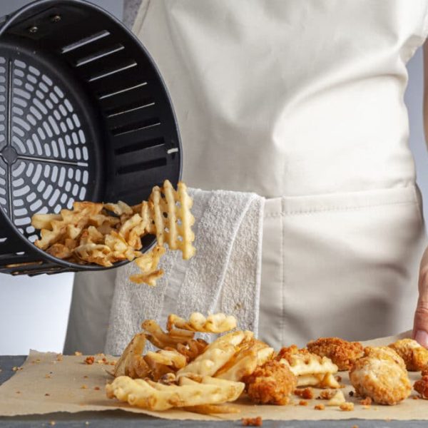 Person holding air fryer basket with fries.