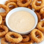 Bowl of sauce surrounded by onion rings.