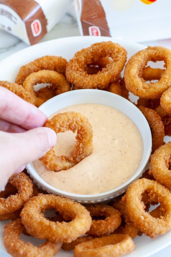 Hand dipping onion ring into sauce. 