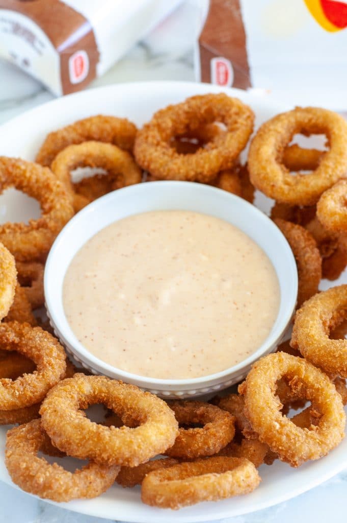 Sauce in a bowl surrounded by fried onion rings. 