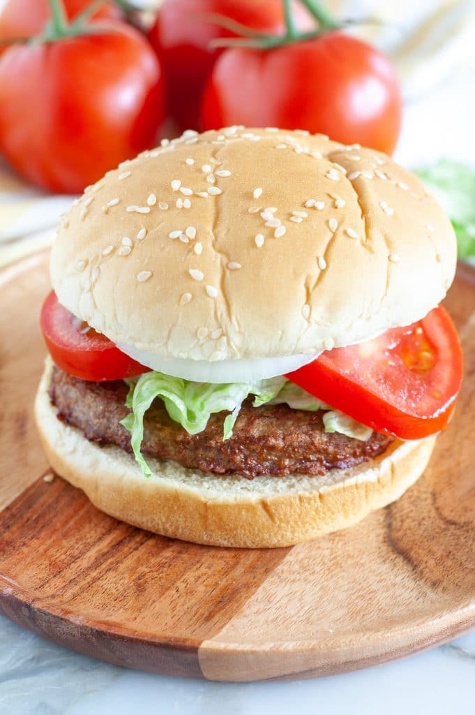 Burger on a plate with tomatoes in background. 