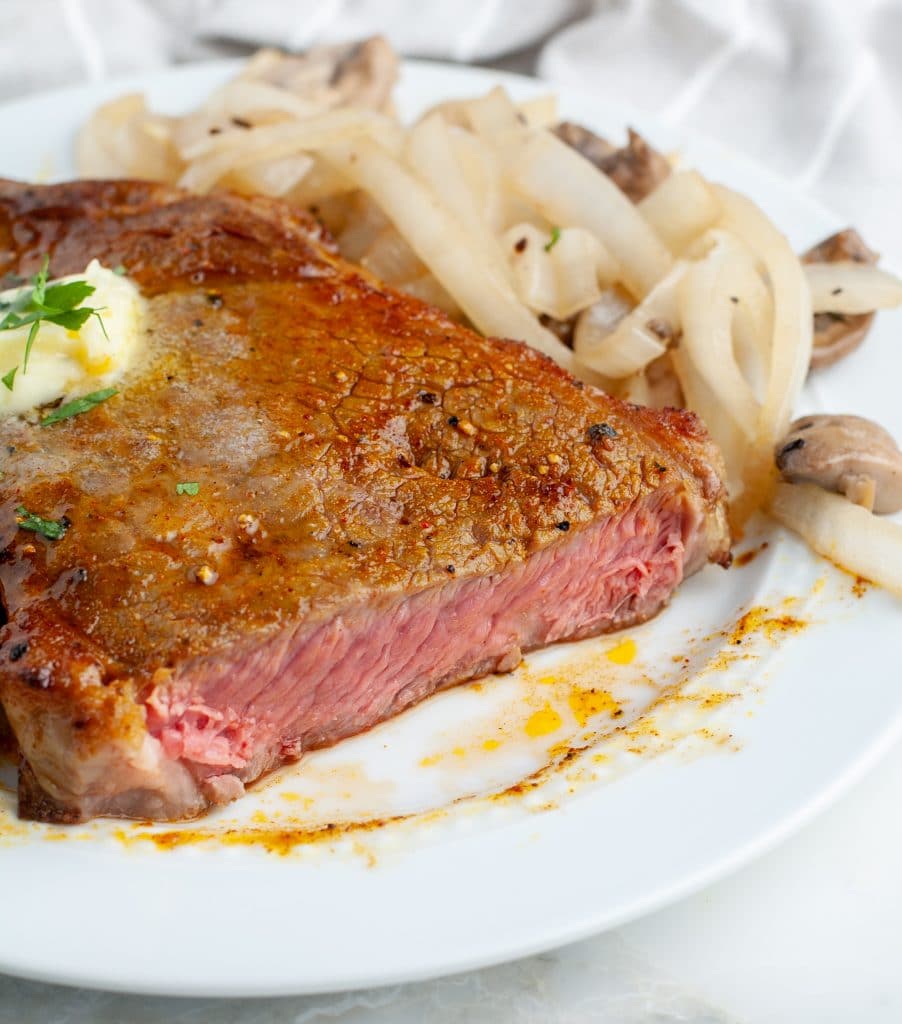 Cut steak on a plate with onions and mushrooms.