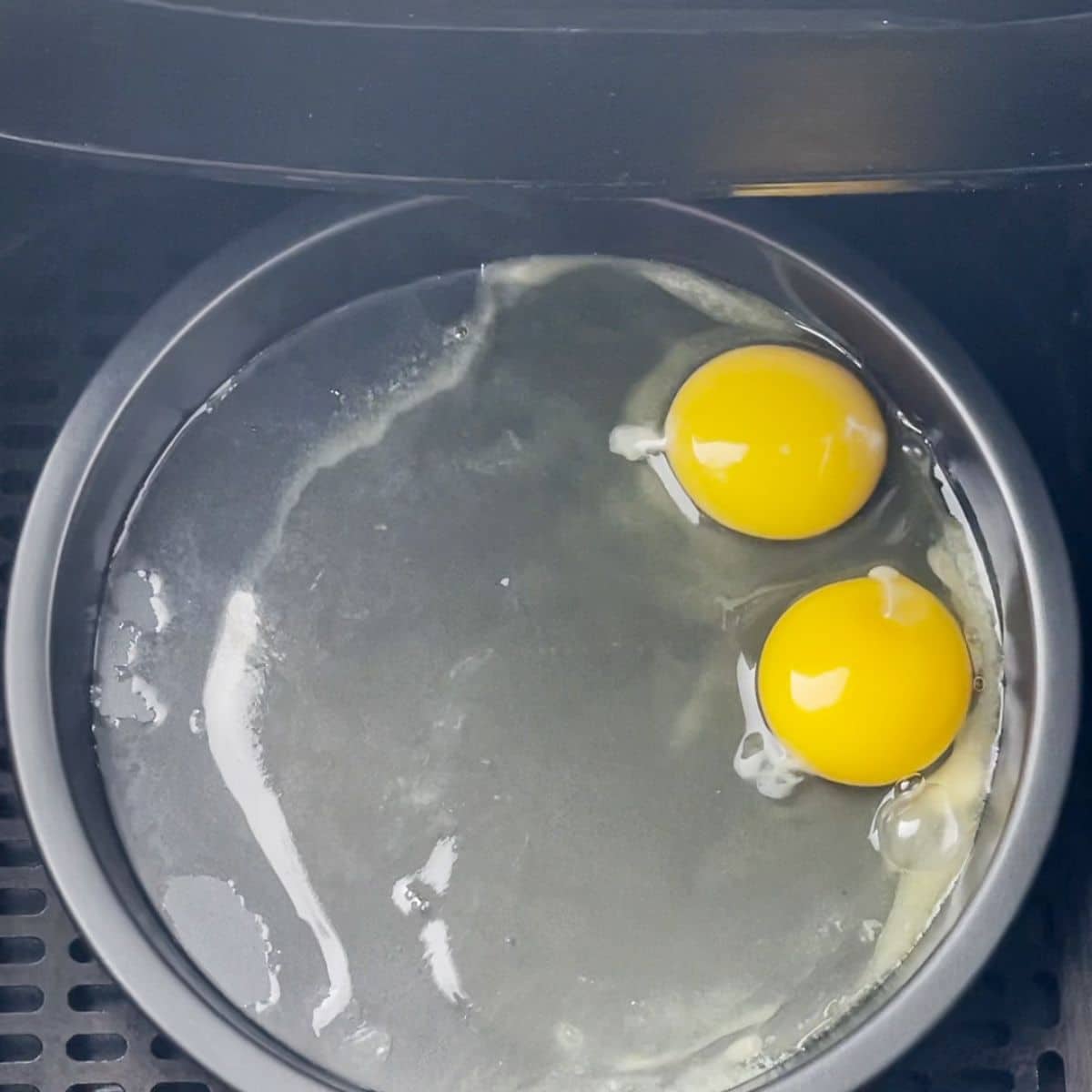 Pan with two eggs in an air fryer basket.