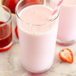 Two glasses of pink milk with strawberries.