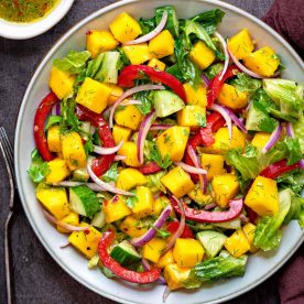 Salad bowl filled with mangos, red onion, and peppers.