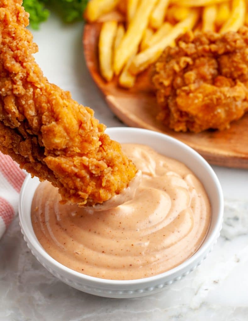 Chicken being dipped into bowl of sauce.