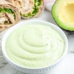 Green dressing in a bowl with chicken wrap.