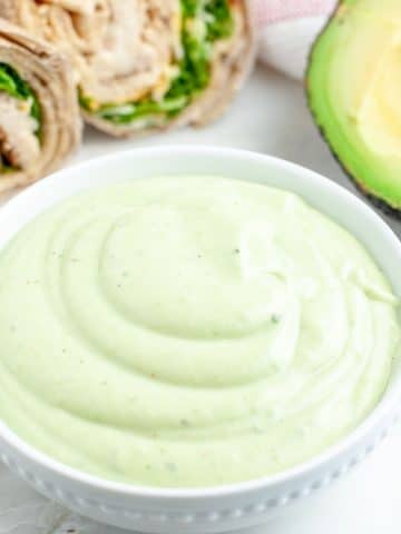 Green dressing in a bowl with chicken wrap.