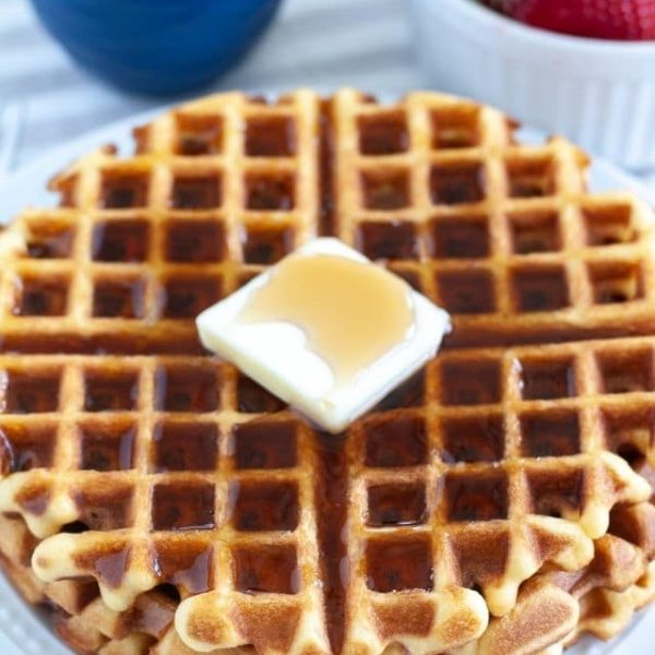 Waffles stacked on plate with butter.