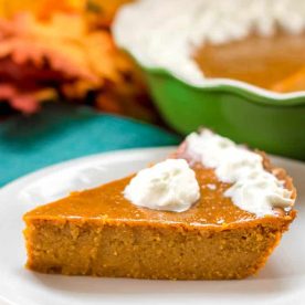 crustless pumpkin pie with a small dollop of whipped cream on top on a white plate. A Green Pie Dish can be seen in the left back corner