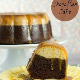 A slice of a chocolate flan site on a plate, the whole flan can be seen on a cake stand in the background