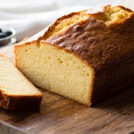 A loaf of pound cake sits on a wooden board along with two slices