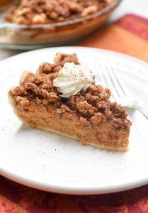 Pumpkin Praline Pie topped with whipped cream sitting on a round white plate