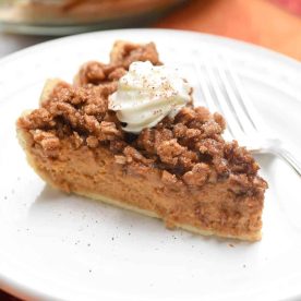 Pumpkin Praline Pie topped with whipped cream sitting on a round white plate