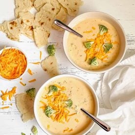 2 white bowls of Broccoli Cheddar Soup garnished with cheese and broccoli.