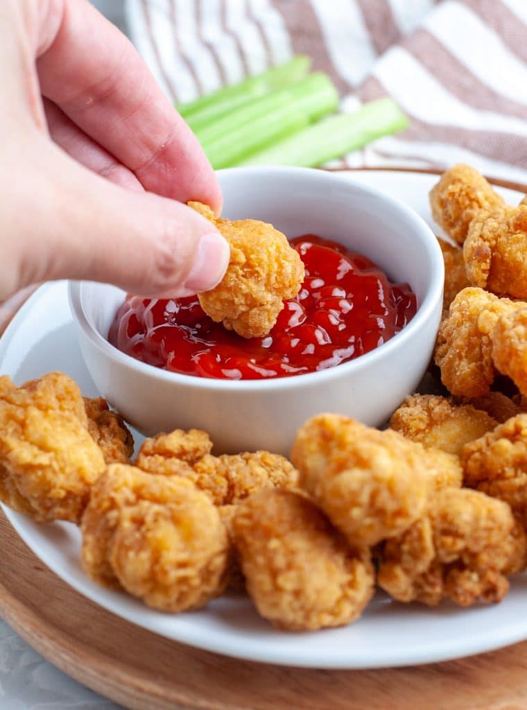 Hand dipping chicken in ketchup.