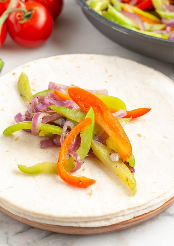 Stack of tortillas with peppers and onions.