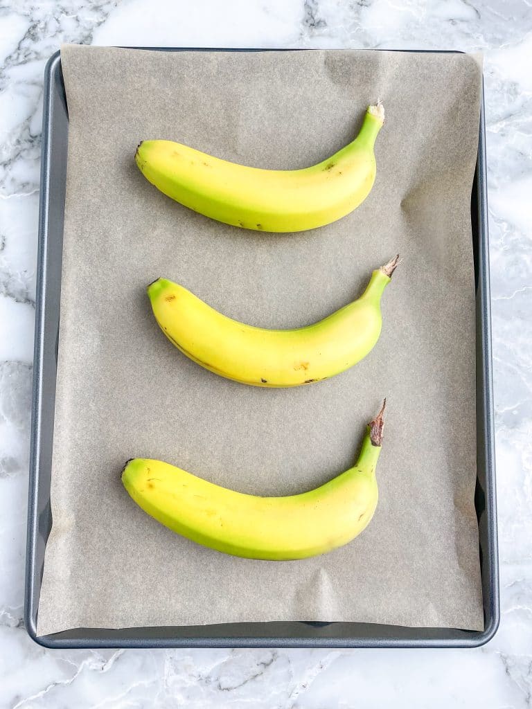 Three bananas laying on lined baking sheet.