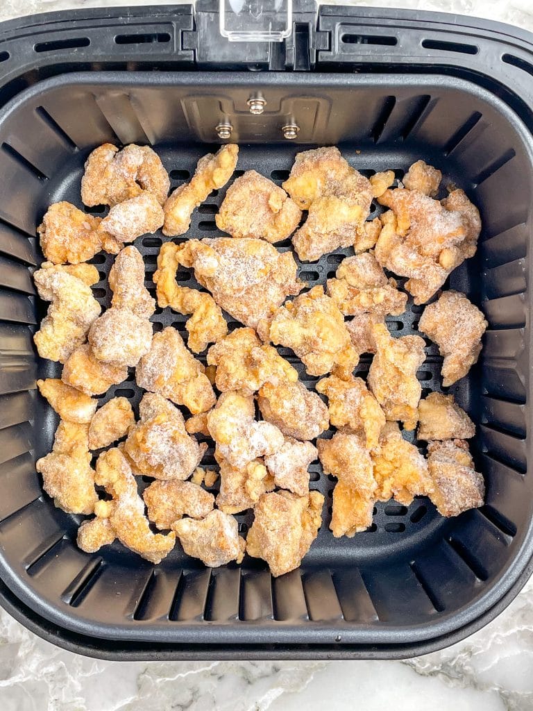 Frozen fried chicken in air fryer basket.