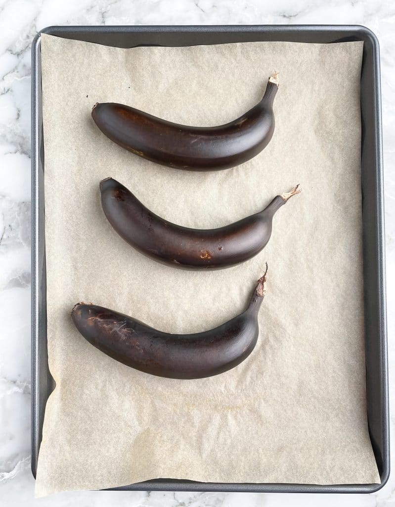 Black bananas laying on lined baking sheet.