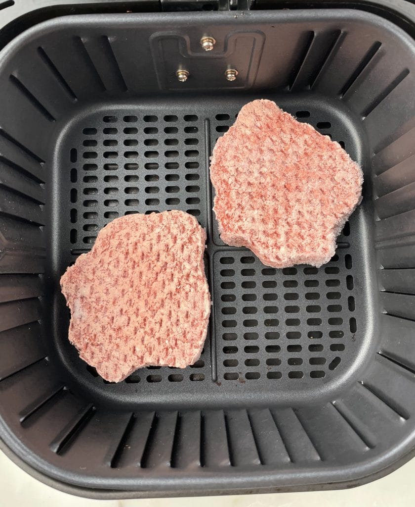 Two frozen hamburgers in air fryer basket.