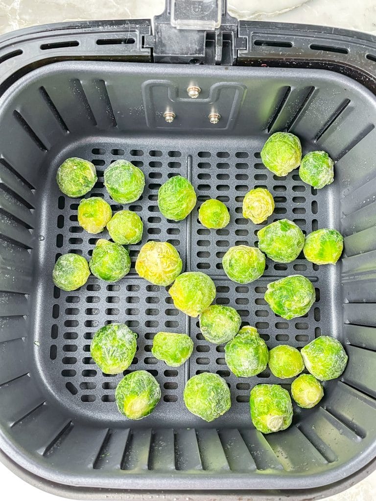 Air fryer basket with frozen brussel sprouts.