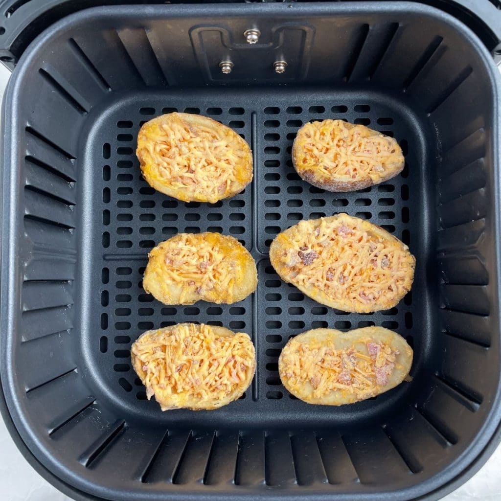 Air fryer basket with frozen potato skins.