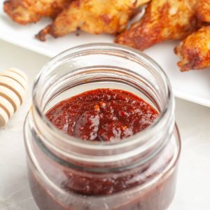Jar of red sauce with chicken wings in the background.