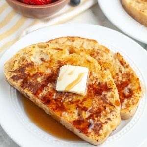 Two pieces of French toast on plate topped with butter and syrup.