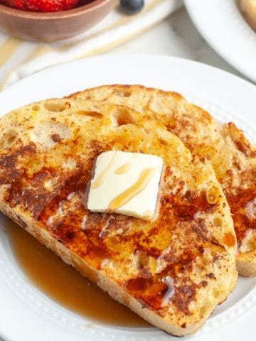 Two pieces of French toast on plate topped with butter and syrup.