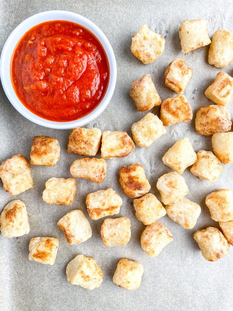 Plate of cooked gnocchi with bowl of red sauce.